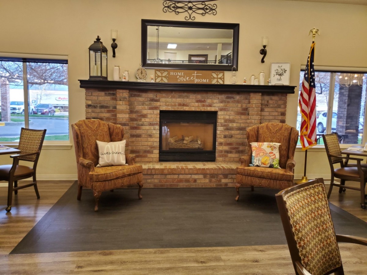 A cozy living room setup featuring a brick fireplace with two wicker chairs adorned with decorative pillows, and an American flag standing in the corner.