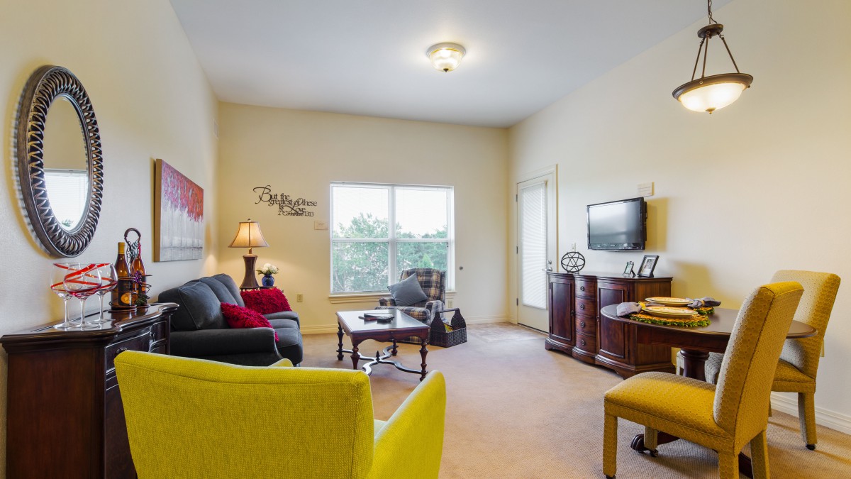 A spacious living room featuring a sofa, armchair, coffee table, and a television with large windows providing plenty of natural light.
