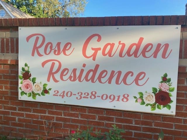 A sign for the Rose Garden Residence with a contact number, displayed on a brick wall.