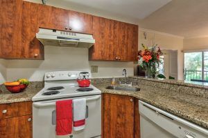 A cozy kitchen with wooden cabinets, a stove with red and white towels, and a granite countertop featuring a sink and flowers.