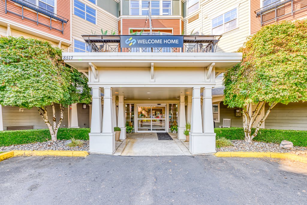 Front entrance of a residential building with a welcome sign and surrounding greenery.