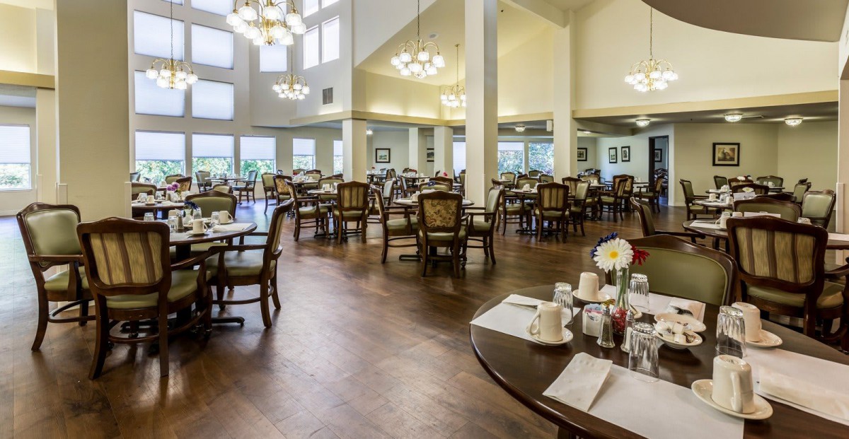 A spacious dining room with elegantly set tables and chandeliers.