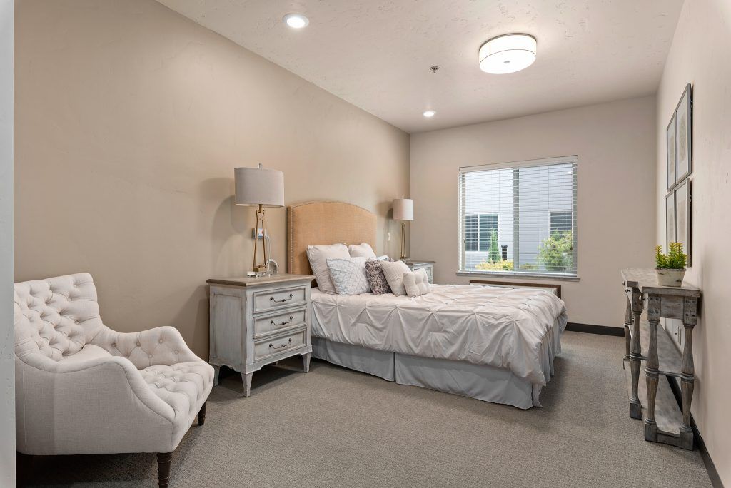 A modern and elegantly decorated bedroom with a bed, side tables, lamps, and a comfortable chair by the window.