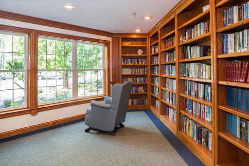 A peaceful reading nook featuring a comfortable armchair and well-stocked bookshelves, bathed in natural light from a large window.