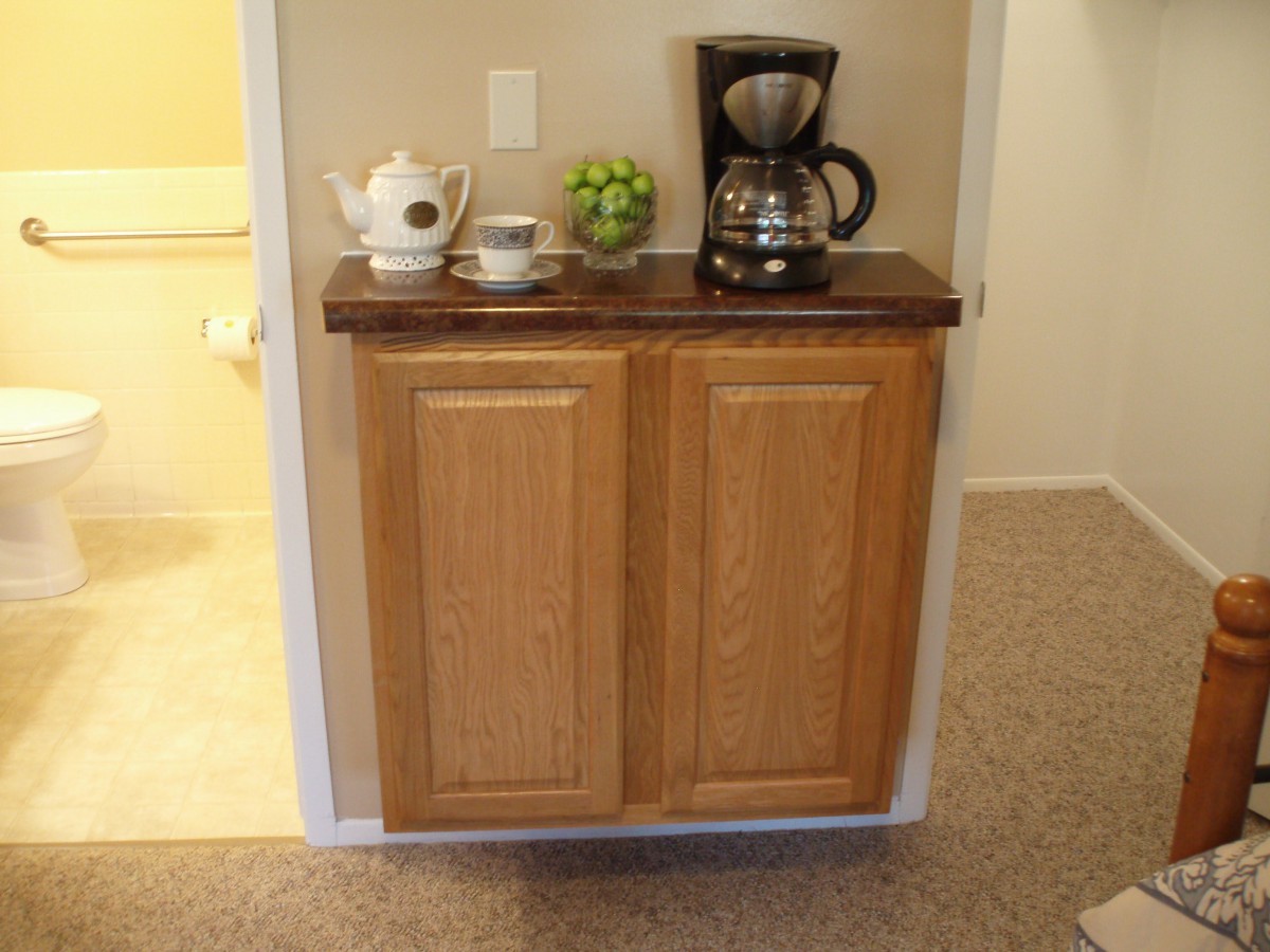 A small kitchen setup with a cabinet featuring a coffee maker, teapot, and cups on top.