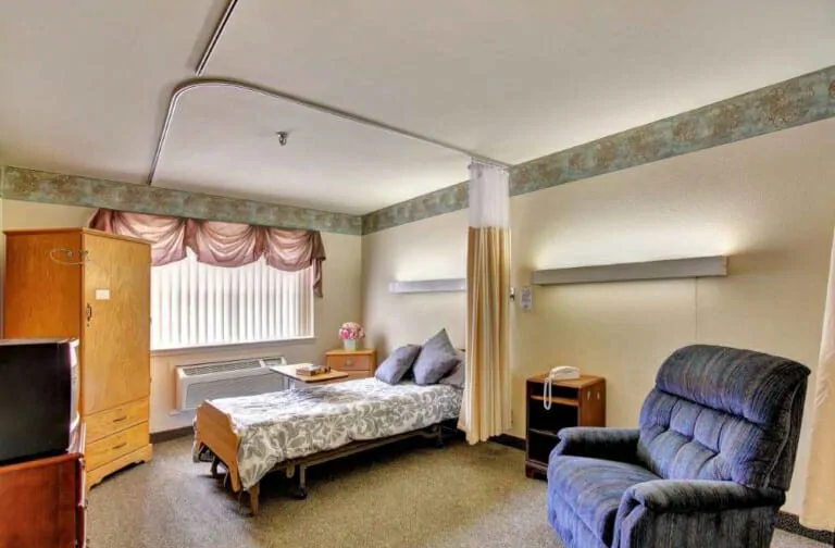 A tidy hospital room with a bed and chair, featuring a window and curtain.