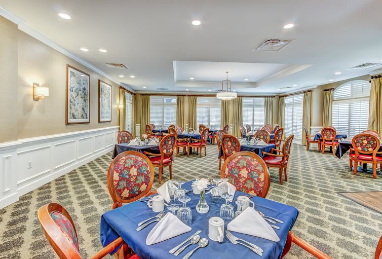 An elegantly set dining room with formal table settings and ornate chairs.
