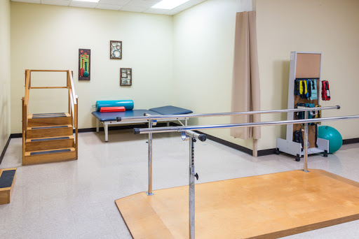 A well-equipped physical therapy room featuring parallel bars and a treatment table.