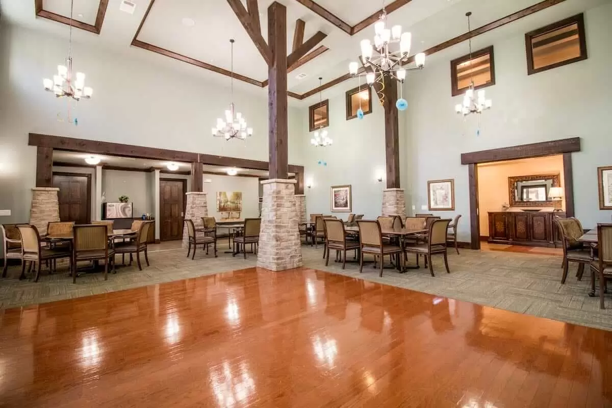 A spacious dining hall with chandeliers, wooden floors, and elegantly arranged tables and chairs.