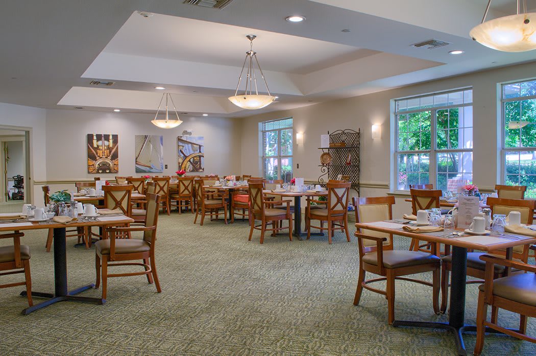 An empty dining room with neatly arranged tables and chairs, well-lit with natural light and ceiling fixtures.