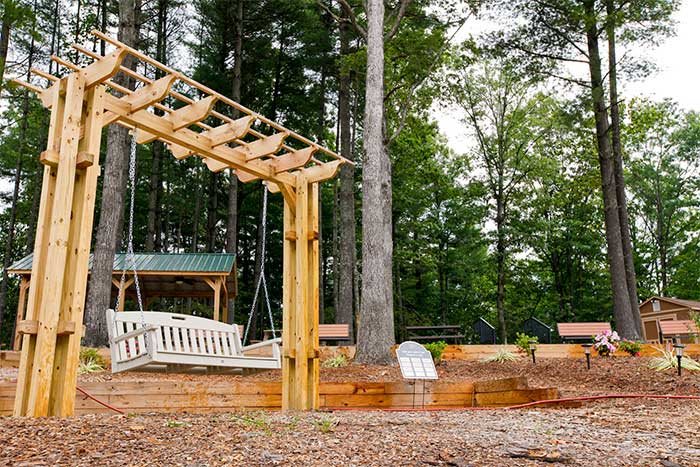 A peaceful outdoor setting featuring a wooden pergola swing among tall trees.