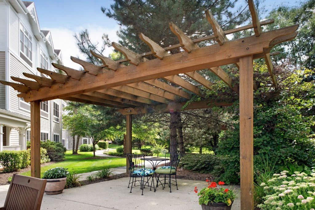 Wooden pergola over a patio area with outdoor seating in a lush garden.