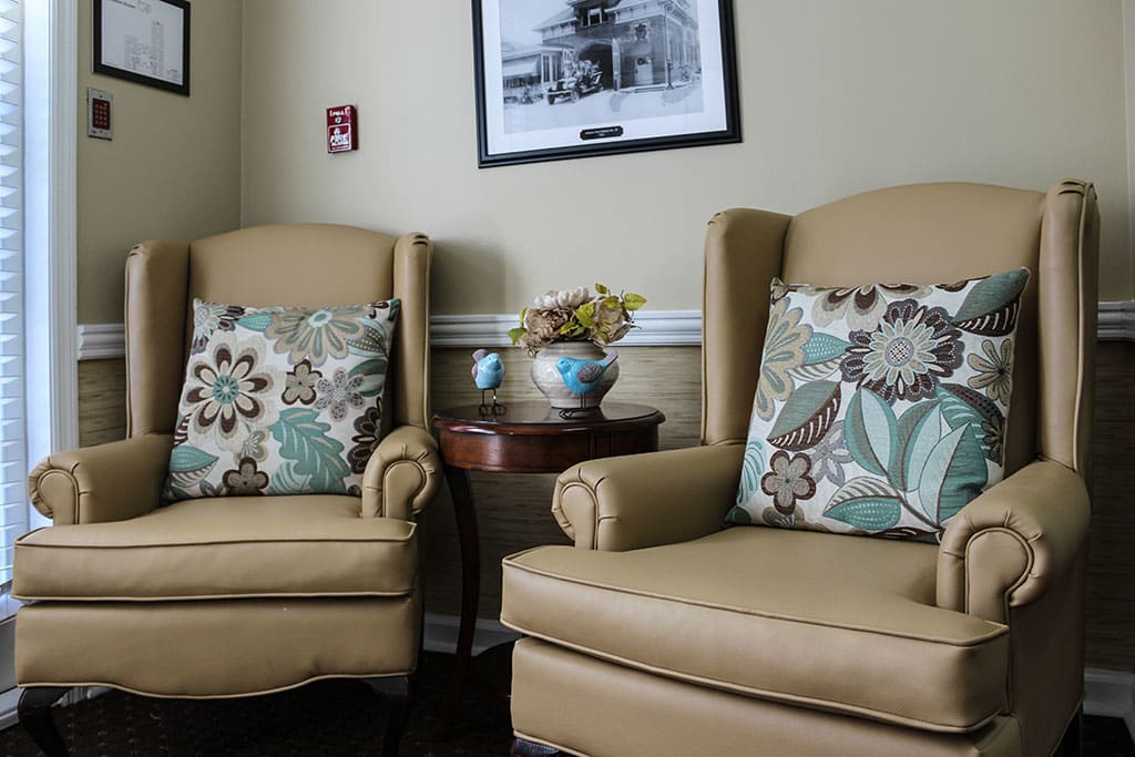 A cozy seating area with two armchairs, floral pillows, and a small table with a flower vase.