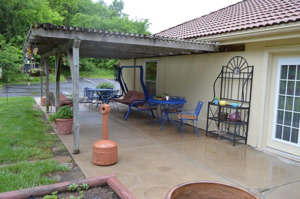 A cozy outdoor patio with a swing chair, tables, and potted plants under a covered area.