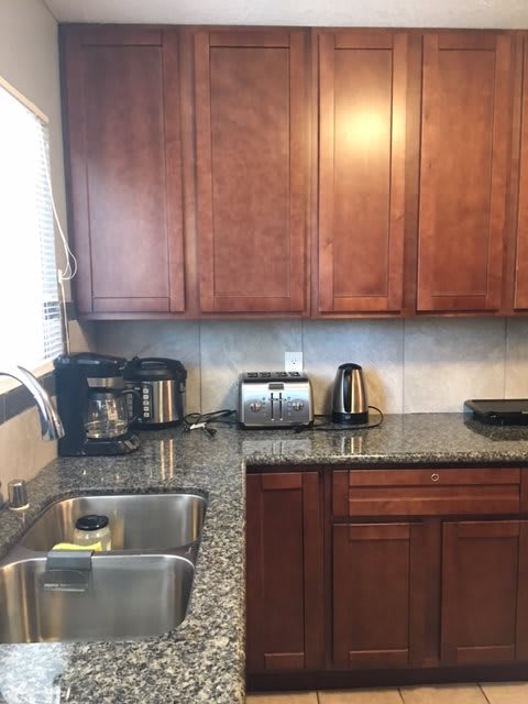 A modern kitchen with wooden cabinets and various appliances on the granite countertop.