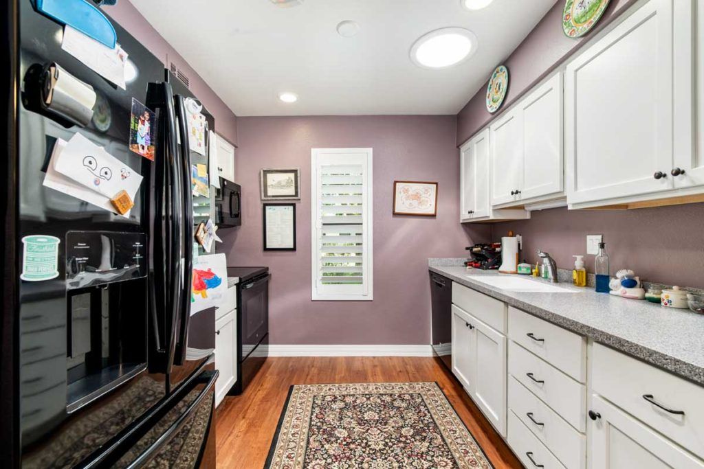 A modern kitchen with purple walls, featuring black appliances, white cabinets, and a decorative rug.