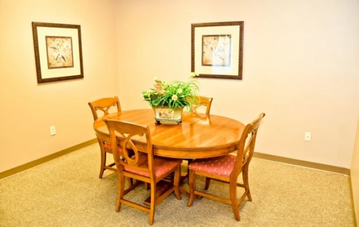A cozy dining room with a round wooden table surrounded by four chairs, decorated with a potted plant and framed artwork on the walls.