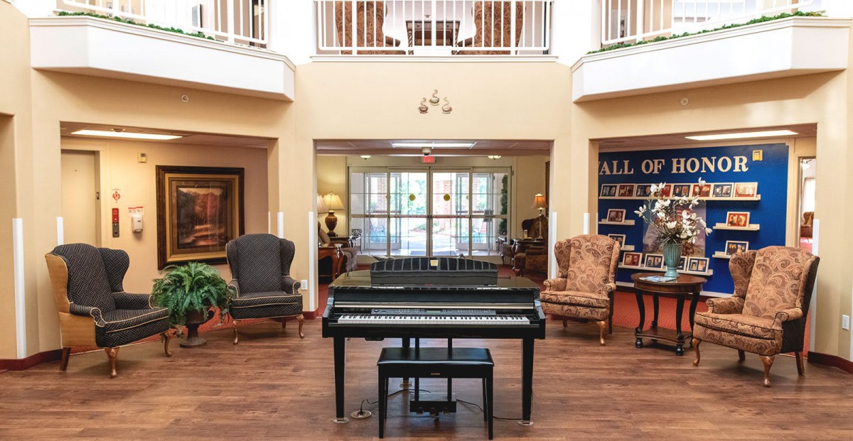A spacious lobby featuring a central piano, surrounded by elegant furniture and natural lighting.
