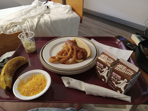 A hospital meal served on a tray featuring pasta, onion rings, a side of cheese, and chocolate milk.