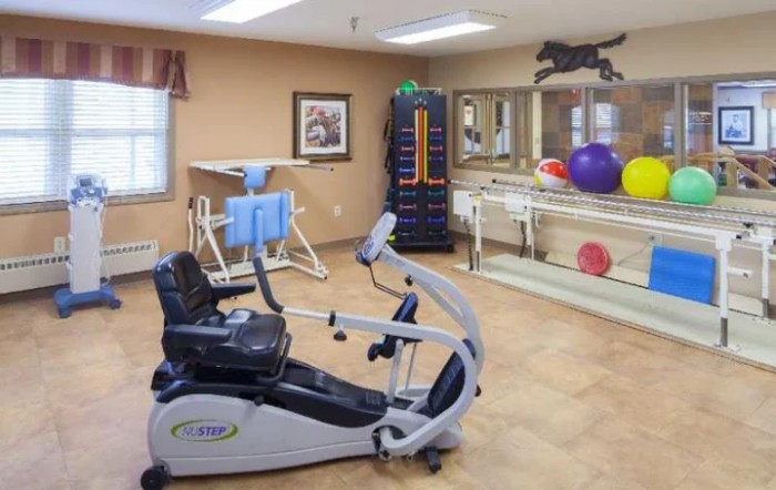 A fitness room equipped with various exercise machines and rehabilitation tools, including a stationary bike and therapy balls.