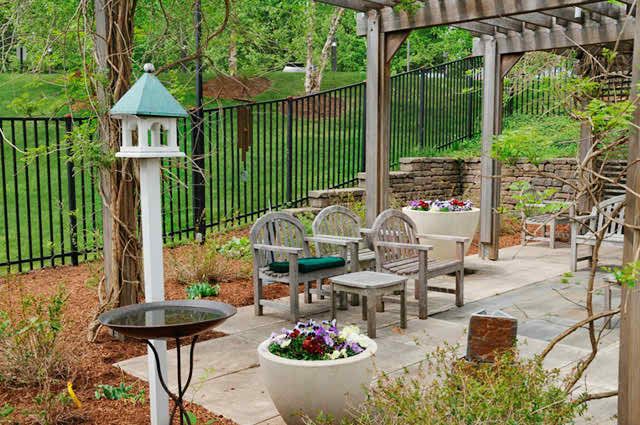 A serene garden setting with outdoor seating, a birdhouse, and vibrant plants under a pergola.