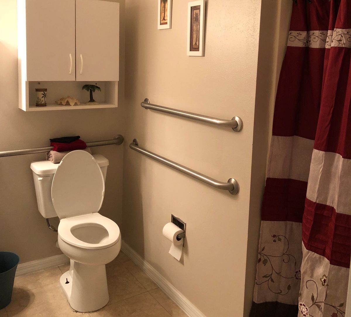 A bathroom featuring a toilet with grab bars, a wall cabinet, and a red shower curtain.