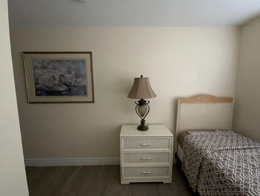 A cozy bedroom corner featuring a bedside table with a lamp, a bed, and wall art.