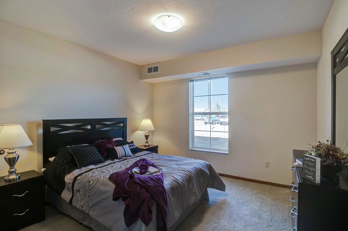 A cozy bedroom with a neatly made bed and a bedside lamp by the window.