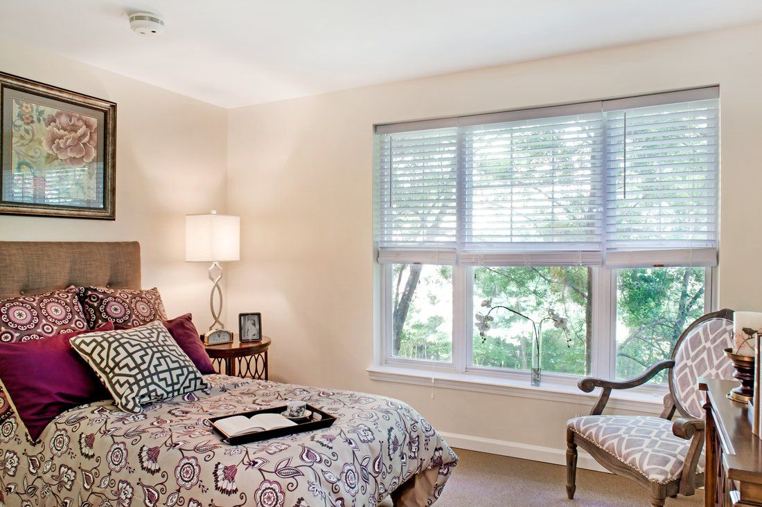 A cozy bedroom with a large window, decorated with patterned bedding and soft lighting.