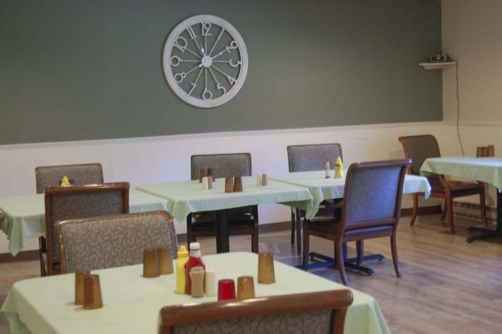 An empty dining room with neatly arranged tables and chairs, featuring a decorative wall piece.