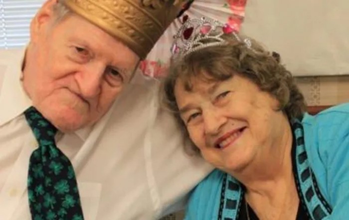 An elderly couple wearing crowns, smiling and celebrating indoors.