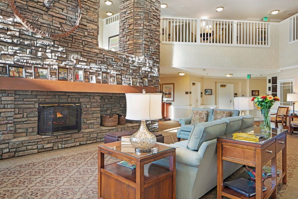 A cozy living room featuring a stone fireplace, comfortable seating, and warm lighting in an open-concept space.