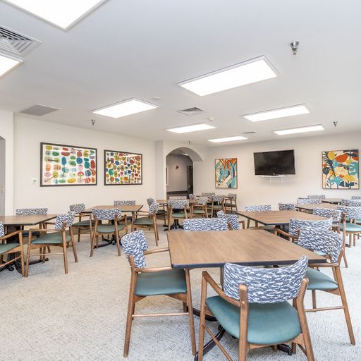 A modern dining room featuring multiple tables and chairs, decorated with artwork on the walls and a television mounted for entertainment.
