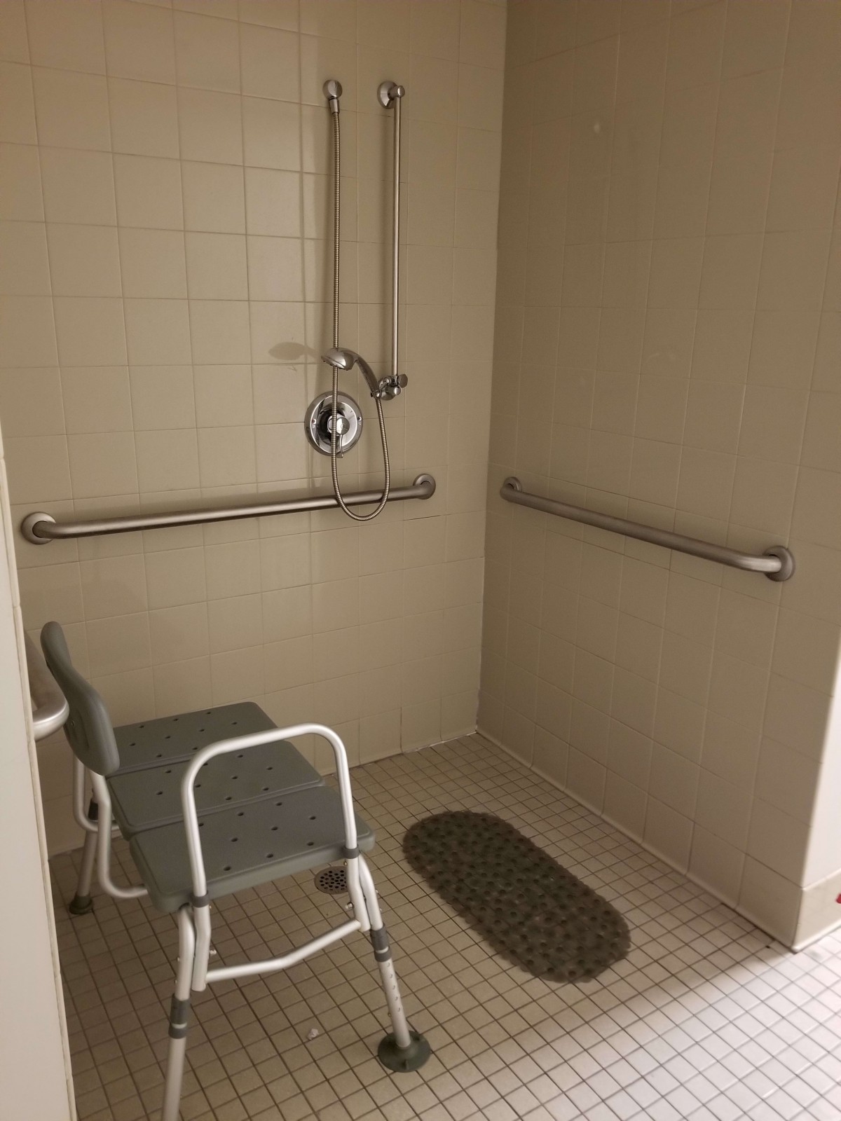 An accessible shower equipped with grab bars, a shower chair, and a non-slip mat for safety.