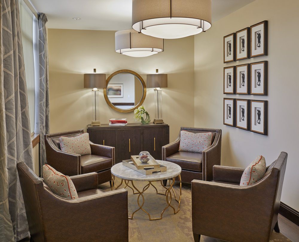 A cozy living room with a modern design, featuring comfortable chairs around a stylish coffee table and accented by soft lighting and wall decor.
