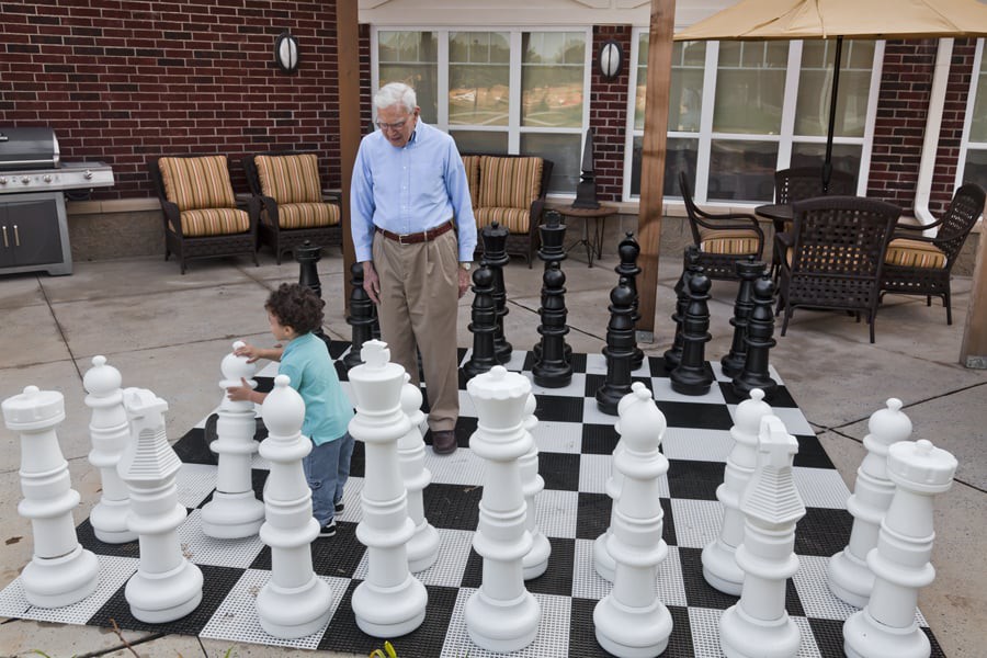 A child and a senior playing on a large outdoor chessboard.
