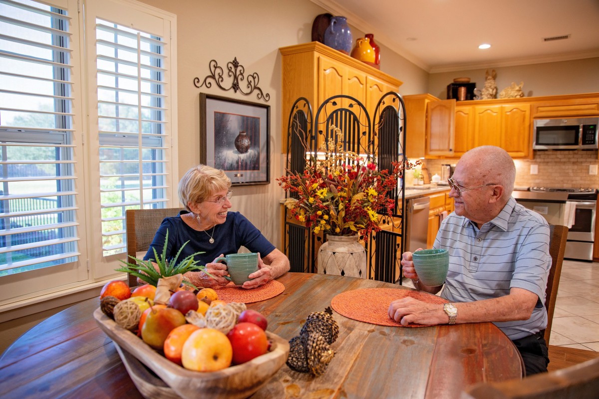 A couple enjoying a conversation over coffee at their kitchen table, surrounded by vibrant home decor and a bowl of fresh fruit.