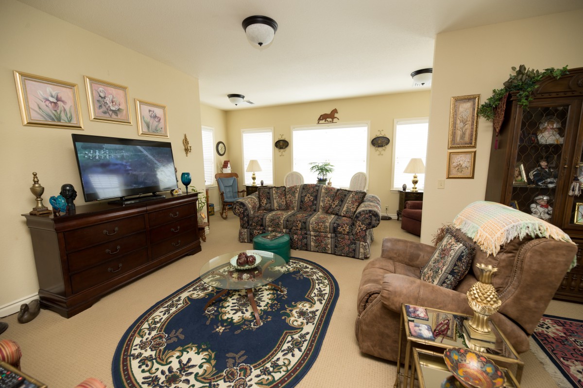 A cozy living room with a patterned carpet, sofa set, armchair, and a television.
