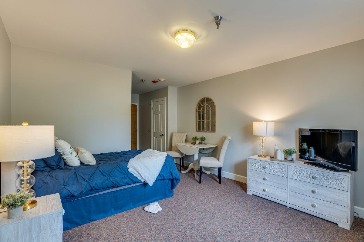 A cozy bedroom with a bed, small dining table, chairs, and a lamp.