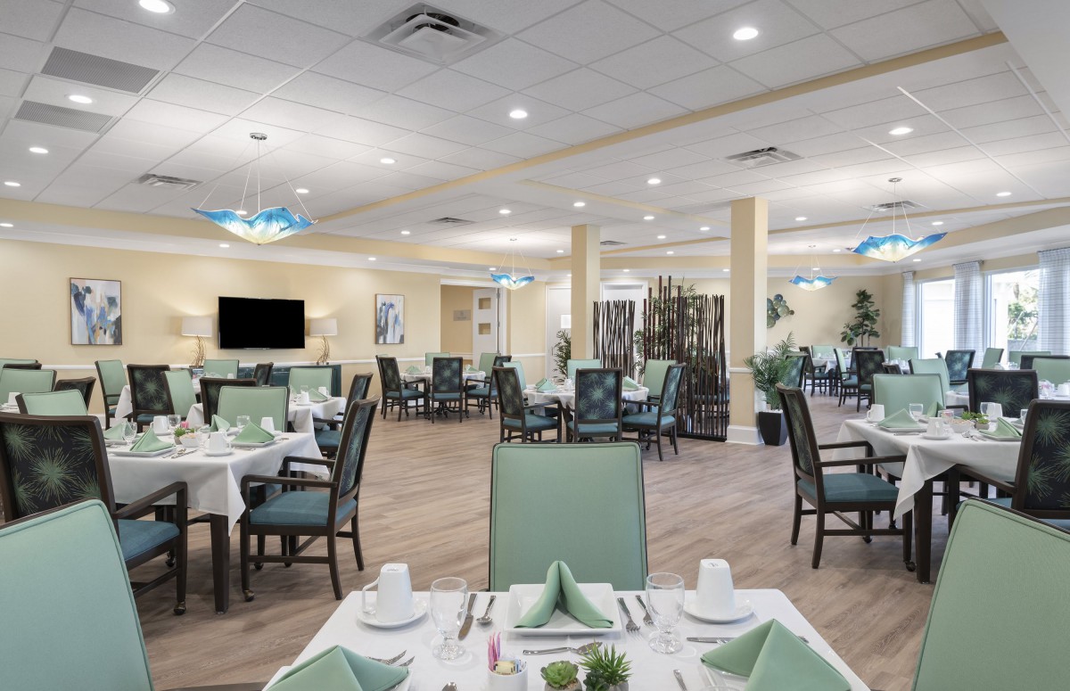 An elegant dining room with neatly arranged tables and chairs, set with place settings under warm lighting.