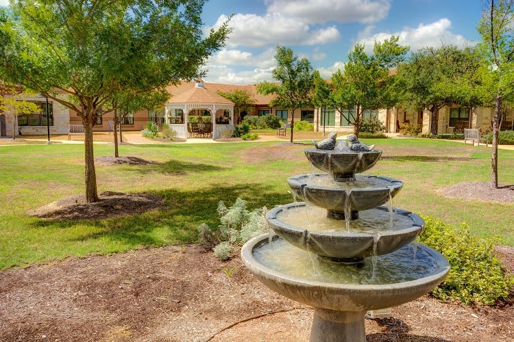 A peaceful garden scene featuring a multi-tiered fountain and a gazebo under a bright blue sky.