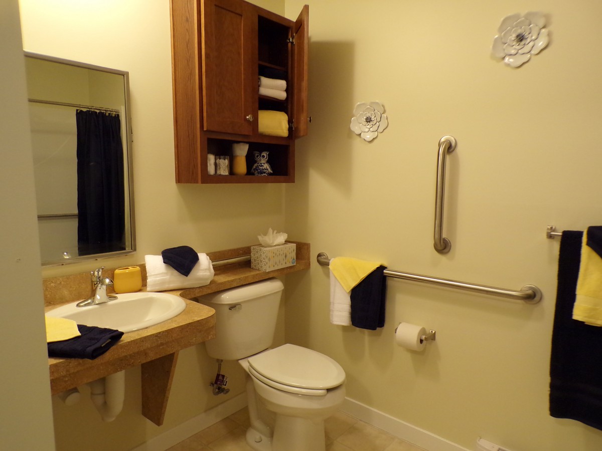 An accessible bathroom with a sink, toilet, cabinet, and grab bar.