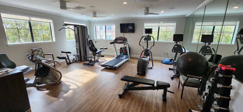 A modern gym with various exercise equipment including a treadmill, exercise bike, and weight bench.