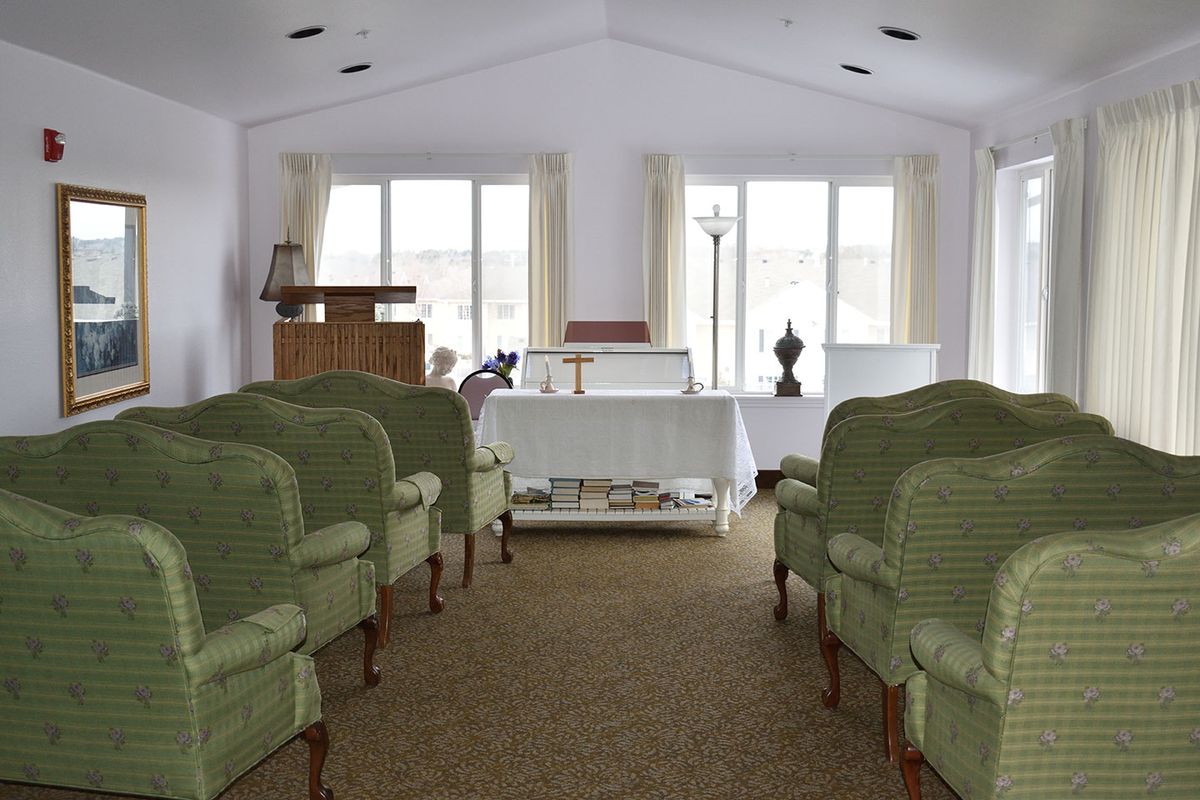 A funeral chapel with rows of green chairs facing a lectern and windows.