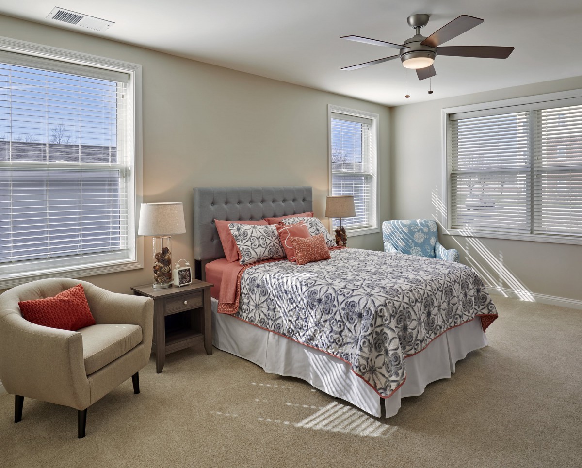 A cozy and well-lit bedroom with a stylish bed and patterned bedding, complemented by natural light from multiple windows.