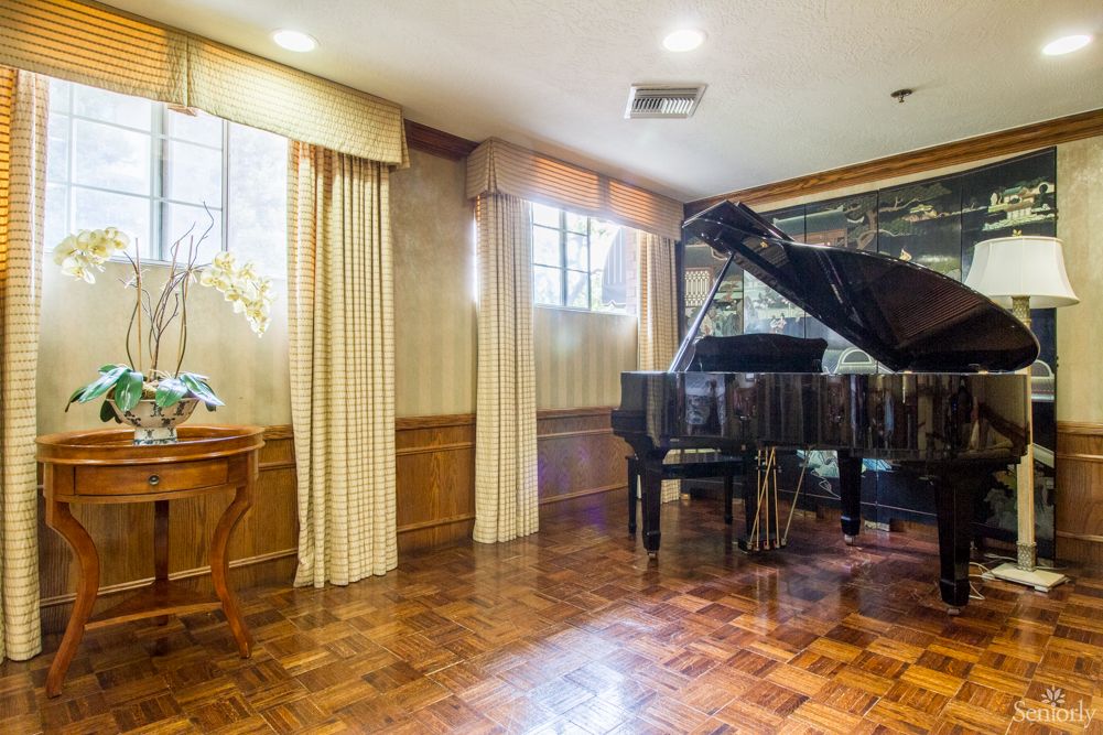 A cozy music room featuring a grand piano on a parquet floor, adorned with curtains and wood paneling.