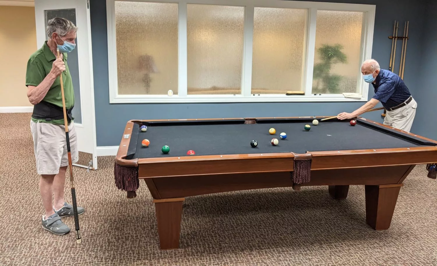 A pool table set up in an indoor game room with a blue wall and carpeted floor.
