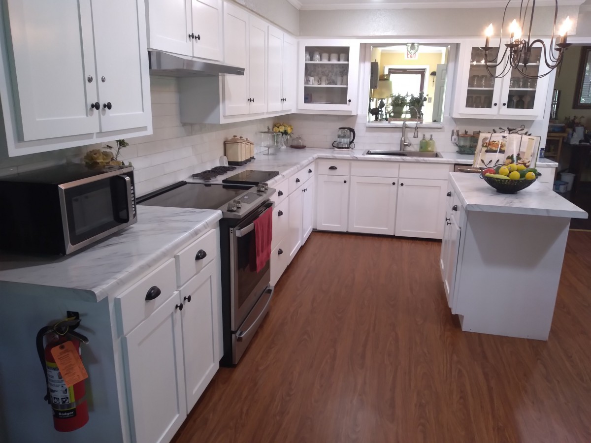 A modern kitchen with white cabinets, a hardwood floor, and various appliances.