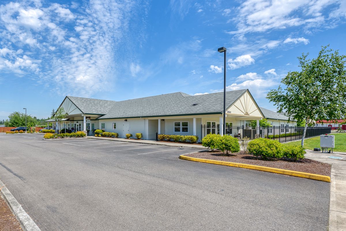 A single-story building with a parking lot under a blue sky with clouds.