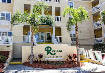 Entrance to the Riviera apartment complex with palm trees and landscaping.
